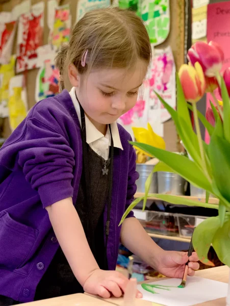 A young girl painting some tulips at a desk in a classroom